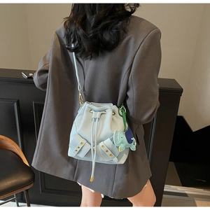 Light blue drawstring bucket bag with litchi grain leather and elephant charm on a model