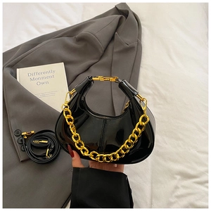 Detail of black patent leather crescent bag featuring a gold chunky chain and metal handle