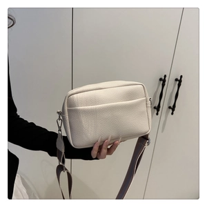 Detail of lychee textured cream PU crossbody bag with adjustable wide fabric strap