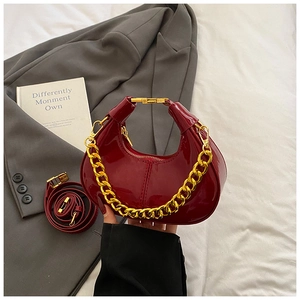 Detail of burgundy patent leather crescent bag with chunky gold chain on a grey blazer