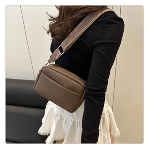Detail of brown litchi pattern leather crossbody bag with colorful striped wide strap