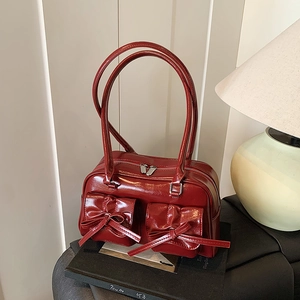 Deep red patent leather bowling bag with bow details and glossy finish in a lifestyle setting