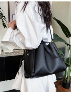 Detail of black lychee grain leather tote bag with gold hardware worn by model