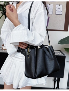 Detail of black lychee grain leather handbag with gold hardware on a female model