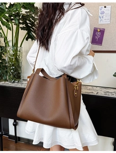Detail of dark brown pebble leather shoulder bag with side wing design and gold hardware