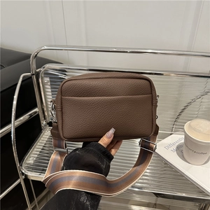 Dark brown pebbled leather crossbody bag with wide striped strap shown in hands