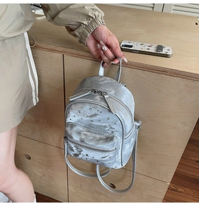 Detail showing hand holding a silver quilted mini backpack with rhinestone embellishments
