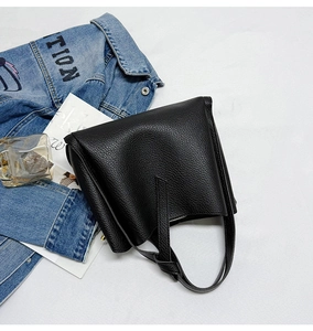 Detail of black lychee grain leather handbag with flap closure on minimalist backdrop