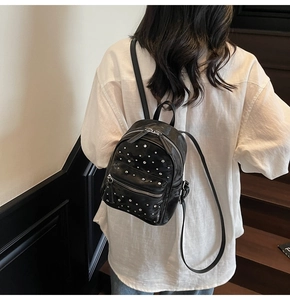 Back view of a black mini backpack with silver studs worn by a model in a white shirt