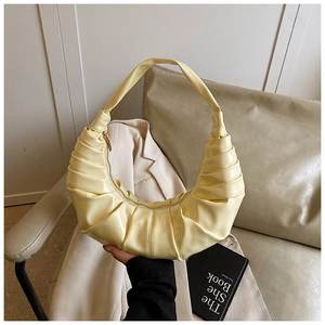 Gros plan du sac plissé jaune crème sur un siège en cuir avec accessoires minimalistes