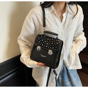 Detail of a black leather mini backpack with silver rivets and fashion text branding