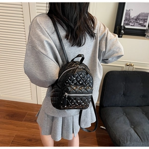 Model wearing a mini black quilted backpack with silver stud accents in a home setting