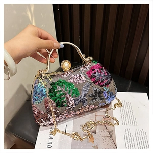 Detail of sequin tropical leaf patterns and gold metal handle on a luxury evening clutch