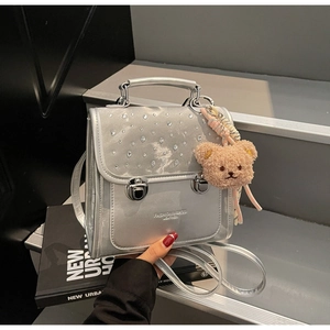 Macro detail of a silver metallic backpack with rhinestones and a brown plush bear charm