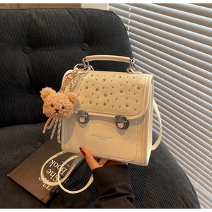 Detail of cream crossbody bag featuring rhinestone flap and brown teddy bear charm