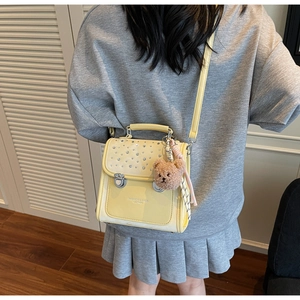 Detail of yellow shoulder bag with sparkling rhinestones and a brown teddy bear charm