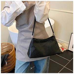Detail of black woven texture shoulder bag with matching strap in a lifestyle setting