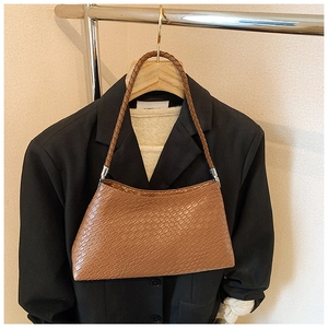 Detail of coffee brown woven leather underarm bag hanging on a suit in a shop