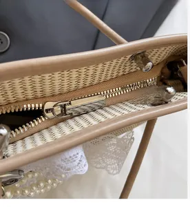 Detail view of smooth metal zipper closure on straw woven handbag with leather trim