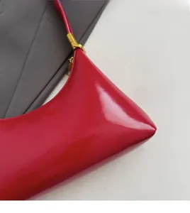 Detail of red crescent bag with glossy finish and gold metal buckle on the side