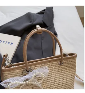 Close-up of woven straw bag with white lace pearl bow and leather handle detail