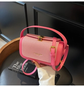 Detail der rosa Lederhandtasche mit Goldverschluss und Webmuster auf einem schwarzen Stuhl