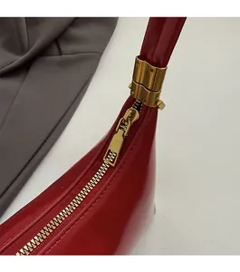 Detail of golden zipper and red patent leather texture on a crescent shoulder bag