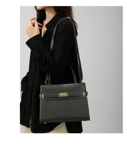 Close-up of black crossbody bag with faux snake texture and gold turn-lock closure