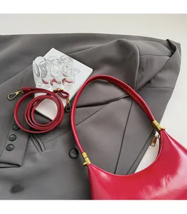 Detail of red patent leather crescent bag with adjustable straps and gold hardware