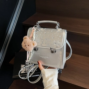 Silver metallic backpack with rhinestones and plush bear charm on wooden steps