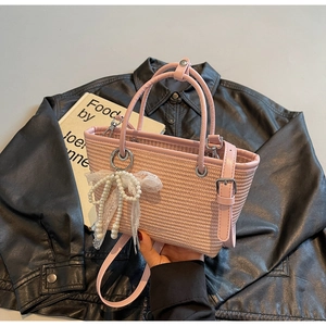 Detailed view of pink woven straw bag with lace pearl bow charm and adjustable handles