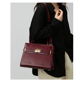 Detail of burgundy leather handbag showing snake-pattern texture and gold twist lock