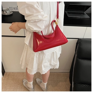 Detail of red crescent shoulder bag featuring glossy patent leather and gold metal buckle