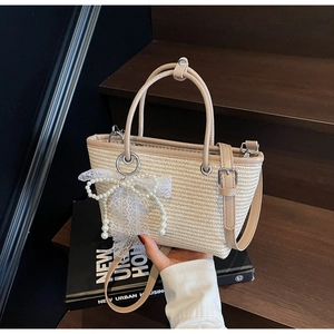 Detail view of woven straw bag with pearl bow, lace accents and leather handles
