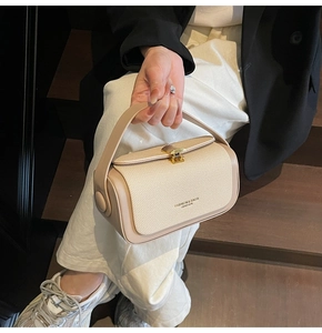 Detail der beige strukturierten Handtasche mit goldenem Drehverschluss und Schriftzug