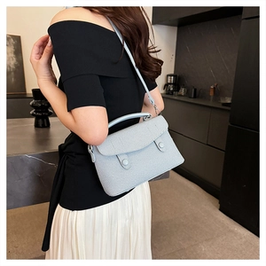 Detailed close-up of light blue textured fabric shoulder bag with twin button decorative flap