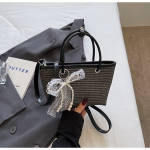 Detail of woven straw tote bag featuring elegant lace bow and pearl charm accents