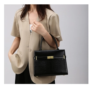 Detail of black trapezoid handbag with croc-embossed leather and gold rectangle twist lock