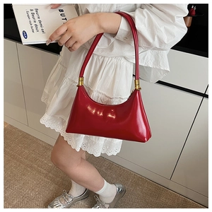 Close-up of red glossy crescent shoulder bag with golden metallic details on a model