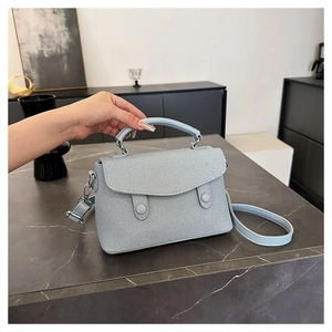Detail of light blue crossbody bag featuring fine twill texture and dual round buckles