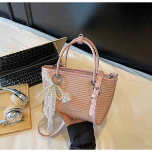 Detailed shot of pink straw handbag with pearl bow charm and leather handles