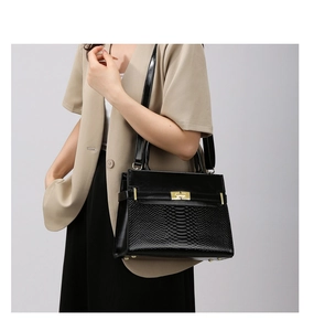 Detail of black crossbody bag with snakeskin texture flap and gold twist lock closure