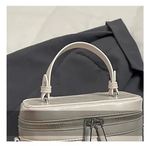 Detailaufnahme des bogenförmigen Tragegriffs und silbernen Reißverschlusses der cremeweißen Tasche