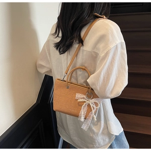 Straw handbag with lace bow and pearl charm shown on model in a vacation style look