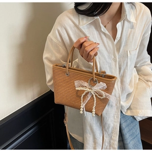 Detail of straw woven handbag featuring lace pearl bow and adjustable shoulder strap