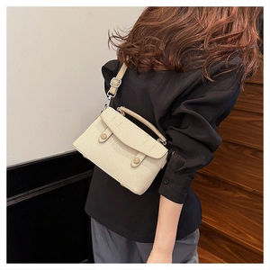 Model wearing a cream woven texture crossbody bag with double cylinder buckle detail