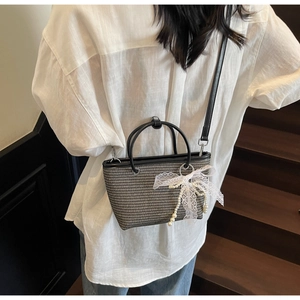 Detail of woven crossbody bag with black leather handles and white lace bow ornament