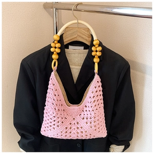 Sac à main en crochet rose ajouré avec de grosses perles en bois jaunes sur un costume