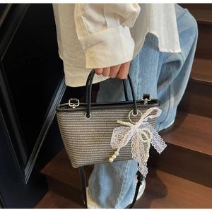Close-up of woven straw handbag featuring black leather trim and white lace bow with pearls