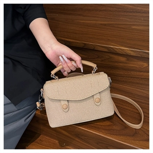 Close-up of beige woven crossbody bag with dual decorative round buckles on the front